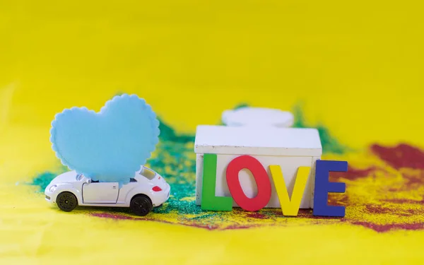 Blue heart on white toy car, alphabet Love on yellow paper backg — Stock Photo, Image