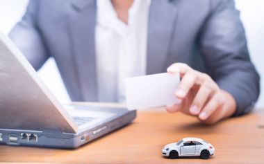 Beyaz kart arka planda tutan bulanık iş adamı oyuncak araba,