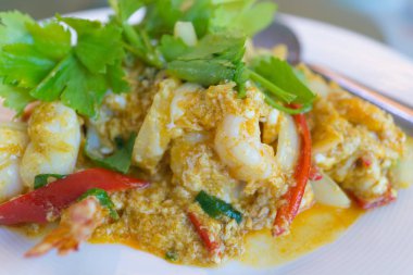 Masada beyaz tabakta köri tozu ile kızarmış karidesi karıştır,