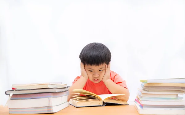 Roztomilý chlapec čtení knihy na stole a bílém pozadí, osvětlené — Stock fotografie