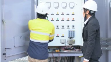 Genç Asyalı mühendis, yönetici mühendis ile birlikte elektrik kontrol kabinesini kontrol ediyor, bir endüstriyel fabrikada, elektrik kontrol kabinesini kontrol eden bir mühendislik konsepti hakkında bilgi veriyor..