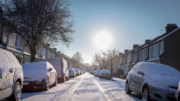 Brittiska gata med bilar och vägen täckt av snö Royaltyfria Stockbilder