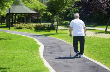 Yaşlı adam bastonla parkta yürüyüş