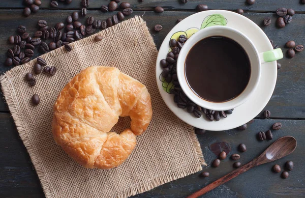 Kaffee und frisch gebackenes Buttercroissant auf dunklem Holzrücken — Stockfoto