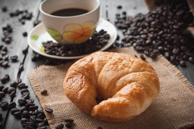 Kahve ve koyu ahşap backgro üzerinde taze pişmiş tereyağı kruvasan