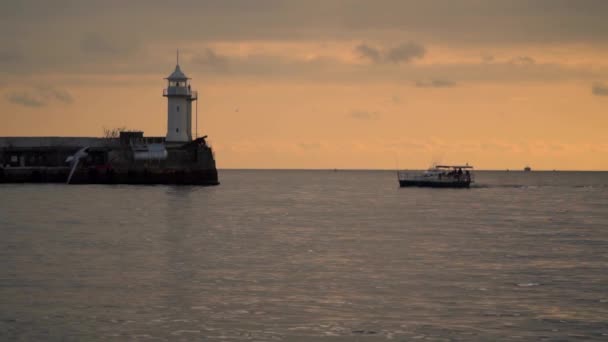 Schwimmt das Boot an der Seebrücke mit einem Leuchtturm vorbei. Abendzeit — Stockvideo