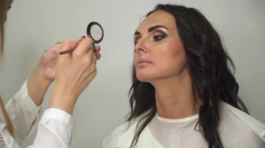 Genç ve güzel kız model sandalyede oturuyor. Makyöz kız makyajı yapar..