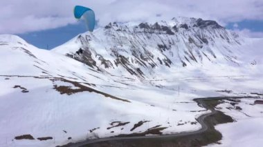 Paraglider karlı dağların arasında uçar. Karla kaplı dağların yanındaki otoyol. Hava görünümü