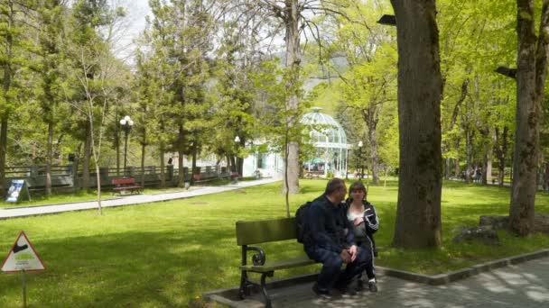 観光客の男性と女性が公園のベンチに座っている 公園はボルジョミに位置しています ボルジョミ Borjoomi ジョージア州南西部のリゾート都市 町はミネラルウォーターで有名です — ストック動画