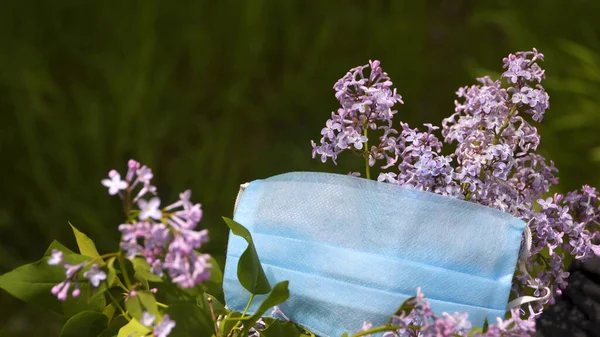 Leylak çiçeklerinin arasında tıbbi maske. Sağlık ve güvenlik kavramı, COVID 19 koronavirüs karantinası, virüs koruması
