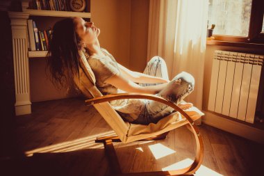 Rahatlatıcı ve pencere radyatör, oturma yanında rahat modern sandalye içinde uyuklayan bir kadın. Sıcak doğal ışık. Rahat ev. Casual giyim. Rahat tarzı kapalı. Oda iç. Yorgun ve düşünceli bir kadın.