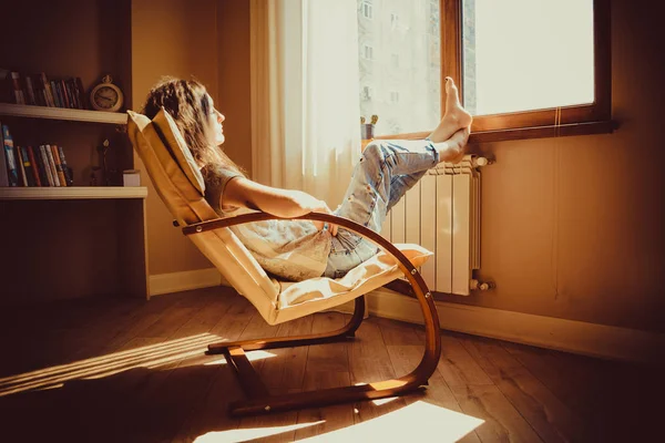 Conceito atencioso. Mulher triste perdido em pensamento descansando em confortável cadeira moderna olhando para a janela na sala de estar. Luz natural quente. Uma casa acolhedora. Estilo casual interior. Interior da sala. Mulher cansada . — Fotografia de Stock