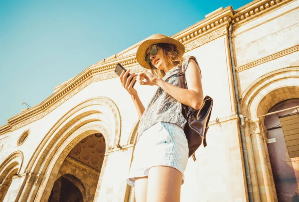 Young woman tourist in hat with backpack using gps navigation on phone. Online booking. Summer fashion style. City tour. Explore the world. Time to travel. Modern technology. Tourism concept. Yerevan — Stock Photo, Image
