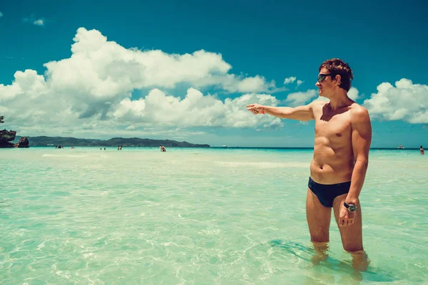 Homem caucasiano mostrando direção com o dedo desfrutando de férias na praia de verão. Hora de viajar. Sem stress. Corpo masculino atlético sem camisa. Férias de luxo exóticas. Conceito de turismo. Espaço para cópia. Usar fato de banho — Fotografia de Stock