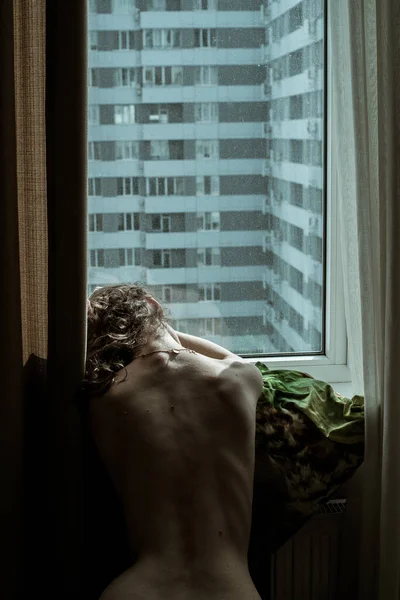 一个赤身裸体的艺术女人坐在一个平整的窗户旁边 呆在家里别动 隔离的概念 Covid 19大流行性大肠癌 住宅区 公寓大楼 社会疏离 — 图库照片