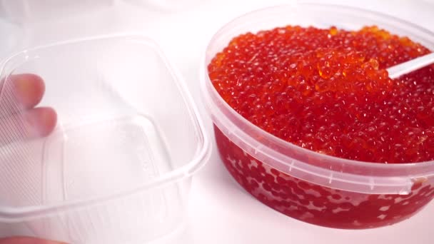 Cuchara tipo caviar rojo. Envase de plástico con caviar salado de salmón sobre fondo blanco — Vídeos de Stock