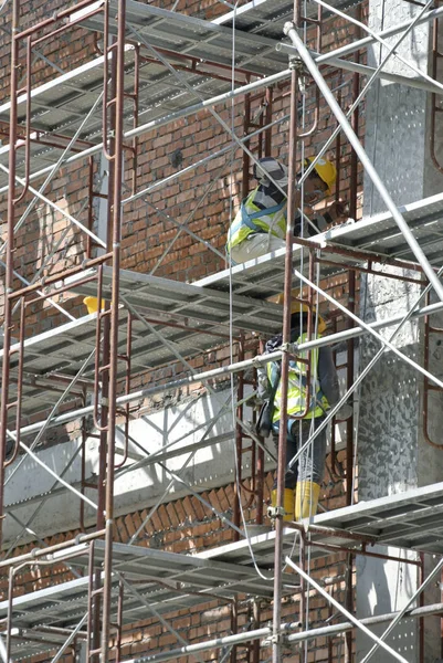 Trabalhadores da construção civil que usam arnês de segurança e instalam andaimes — Fotografia de Stock