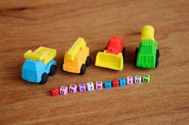 Ahşap doku arka plan üzerinde sentetik kauçuk yapılmış inşaat ağır makine minyatür modeli. Ortadaki küçük plastik blok üzerine basılmış inşaat metni.  