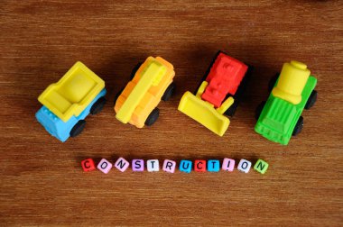 Ahşap doku arka plan üzerinde sentetik kauçuk yapılmış inşaat ağır makine minyatür modeli. Ortadaki küçük plastik blok üzerine basılmış inşaat metni.  