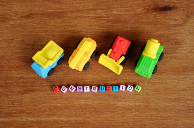 Ahşap doku arka plan üzerinde sentetik kauçuk yapılmış inşaat ağır makine minyatür modeli. Ortadaki küçük plastik blok üzerine basılmış inşaat metni.  