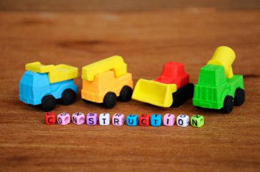 Ahşap doku arka plan üzerinde sentetik kauçuk yapılmış inşaat ağır makine minyatür modeli. Ortadaki küçük plastik blok üzerine basılmış inşaat metni.  