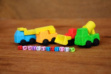 Ahşap doku arka plan üzerinde sentetik kauçuk yapılmış inşaat ağır makine minyatür modeli. Ortadaki küçük plastik blok üzerine basılmış inşaat metni.  