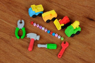 Ahşap doku arka plan üzerinde sentetik kauçuk yapılmış inşaat ağır makine ve inşaat araçları, minyatür modeli. Ortadaki küçük plastik blok üzerine basılmış inşaat metni.  