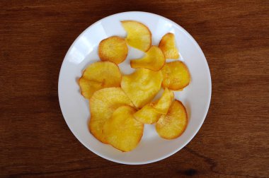 Kurutulmuş ve ahşap doku arka plan üzerinde beyaz plaka üzerinde kızarmış manyok dilimleri yer izole. Bu yerel Malaysian geleneksel abur cubur çağrı havuçlu Ubi mı.