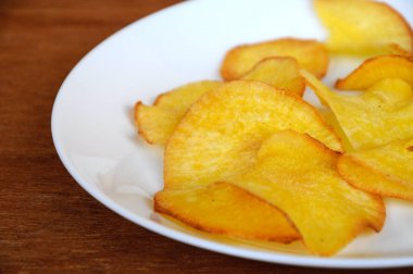 Kurutulmuş ve ahşap doku arka plan üzerinde beyaz plaka üzerinde kızarmış manyok dilimleri yer izole. Bu yerel Malaysian geleneksel abur cubur çağrı havuçlu Ubi mı.