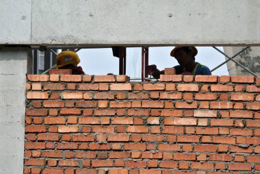 KUALA LUMPUR, MALAYSIA - 14 Temmuz 2016: İnşaat işçileri inşaat sahasına kil tuğla döşeyerek duvar oluşturdular. Tuğla, çimento harcı kullanarak birbirine yapışır.. 
