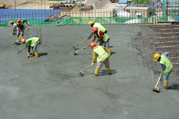 KUALA LUMPUR, MALAYSIA-JANUARY 17, 2017: Строители выравнивают мокрый бетон. В этой работе они также используют вибратор
.