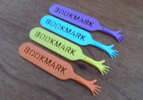 Colorful plastic bookmark used to mark reading location after stop reading the book. It was design with image of colorfull hand and has word \'bookmark\' on it.