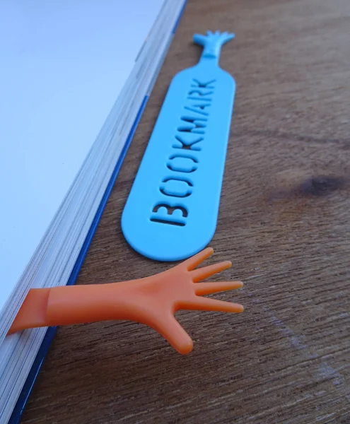 Colorful plastic bookmark used to mark reading location after stop reading the book. It was design with image of colorfull hand and has word \'bookmark\' on it.