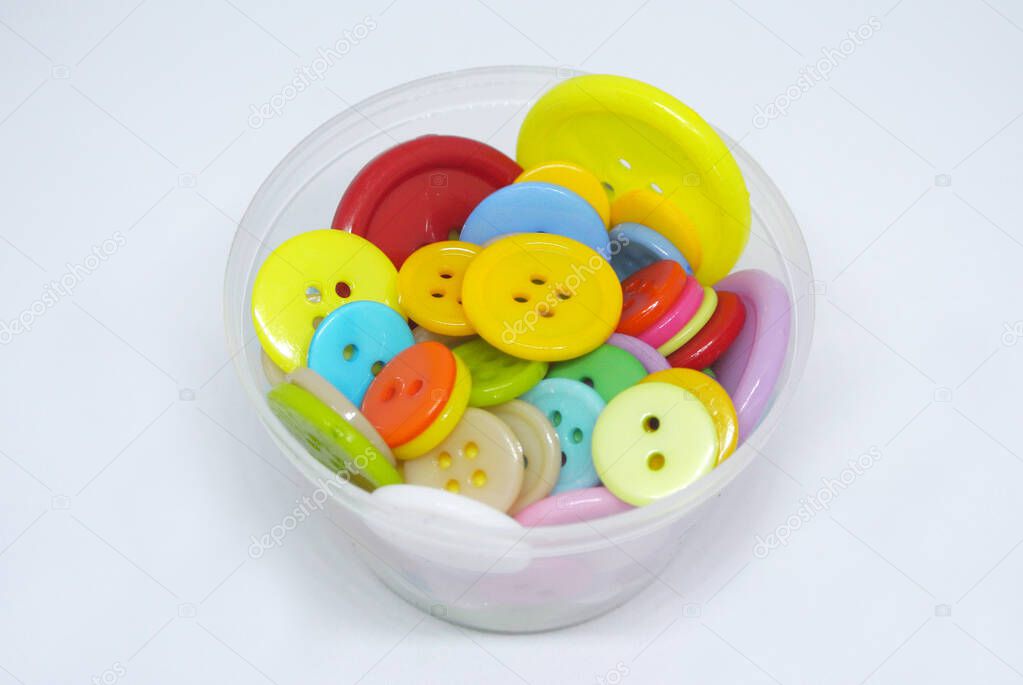Colourful and various size of cloth button inside clear plastic container isolated on white background 