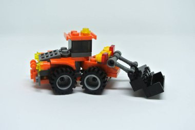 Çoğunlukla turuncu ve siyah plastik tuğlalardan yapılmış oyuncak buldozer. Beyaz bir arkaplanda izole edilmiş.