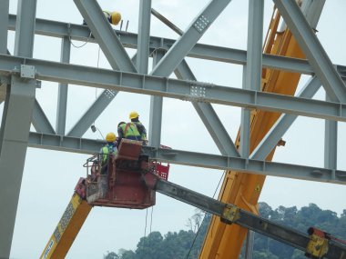 Seremban, Malezya -3 Haziran 2017: İnşaat işçileri inşaat alanında yüksek seviyede çalışırken seyyar vinç kovasında duruyorlar. Uygun güvenlik giysileri giyiyorlar.. 
