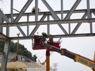 Seremban, Malezya -3 Haziran 2017: İnşaat işçileri inşaat alanında yüksek seviyede çalışırken seyyar vinç kovasında duruyorlar. Uygun güvenlik giysileri giyiyorlar.. 