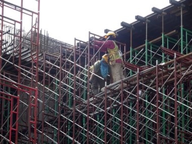KUALA LUMPUR, MALAYSIA -JULY 28, 2019: Construction workers wearing safety gear and safety harness while installing scaffolding at a high level in the construction site.