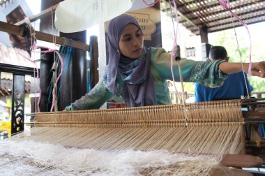 KUALA LUMPUR, Malezya - Kasım 29. 2018: Bir kadın şarkı sözü dokumak için geleneksel dokuma makineleri kullanıyor. Songket, yüksek kaliteli ve değerli geleneksel Malezya giysisidir..