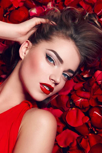 La ragazza in abito rosso sdraiata sul pavimento nei petali di rose rosse . — Foto Stock