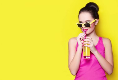 Güzel genç kız Studio sarı bir arka plan ve sarı suyu içme sarı güneş gözlüğü.