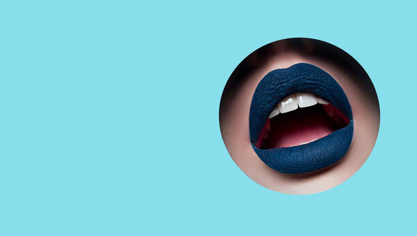 Beautiful plump bright lips with blue matte lipstick look into the circular hole of the colored paper.