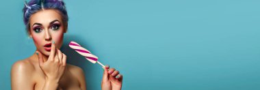 Güzel, genç, neşeli bir kız şaşkınlıkla bakıyor elinde mavi dondurmalı bir boynuz tutuyor. Saç stili - mavi saç. Parlak makyaj. İkram, tatlı, ferahlatıcı tatlılık. Parlak renkler.