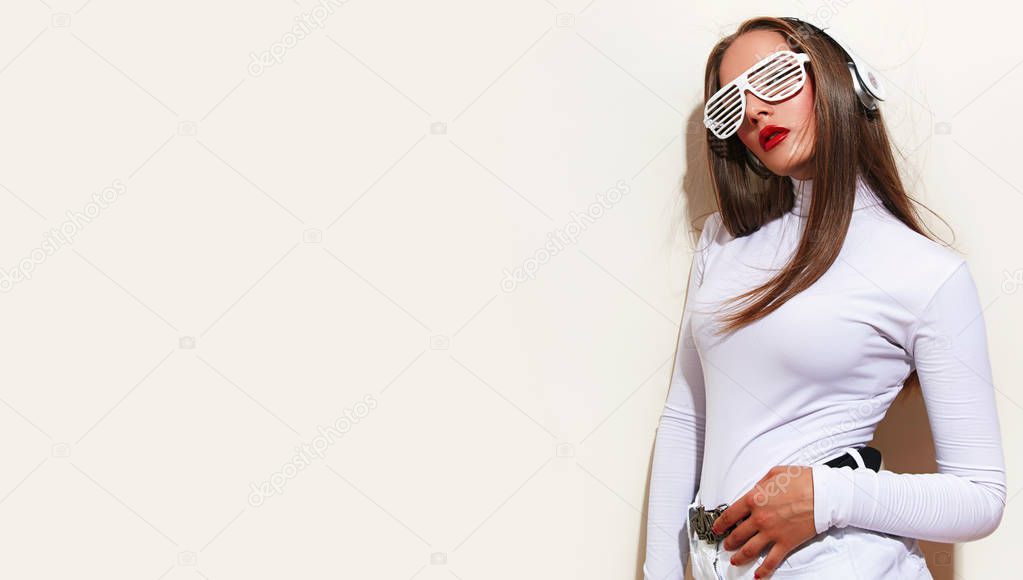 Young beautiful fashionable girl with bright make-up in white glasses with headphones, listening to music. Movement, energy style. 