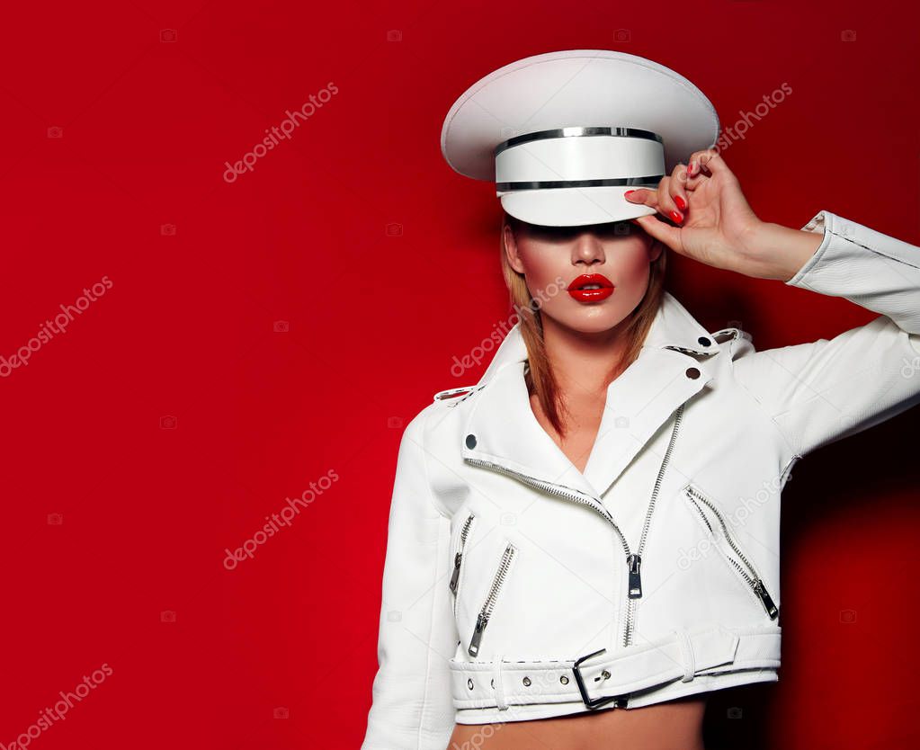 Beautiful young fashionable girl in a white cap and white jacket on a red background with red lips and nails.