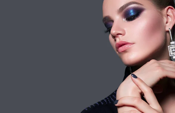 Beautiful young white women close-up in a black jacket on a gray background in the studio. Makeup - blue smokeys, shades of metallic, lipstick bright glossy shine. Hairstyle - smoothly combed hair.