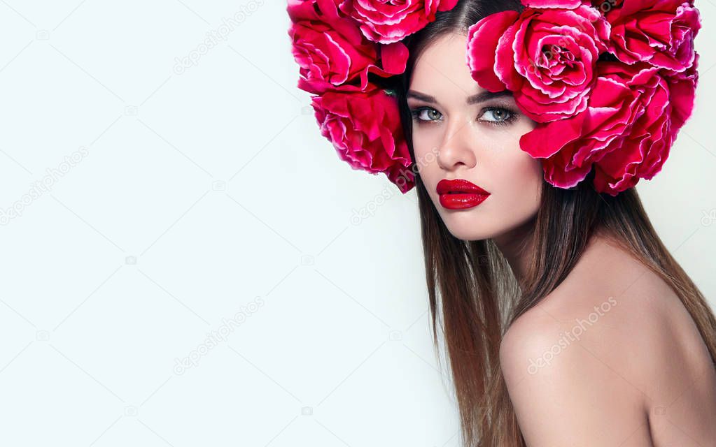 Beautiful girl with a big wreath on the head of a large red roses.Gentle make-up on the face of the girl. Red lipstick on the lips.Portrait of a girl with a crown of flowers in the studio.