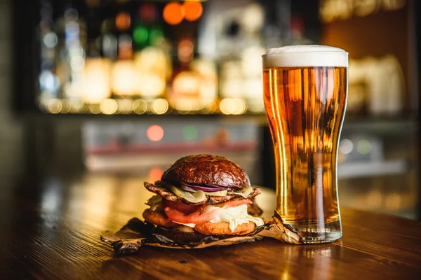 Hamburguesa y cerveza ligera sobre fondo de pub . — Foto de Stock