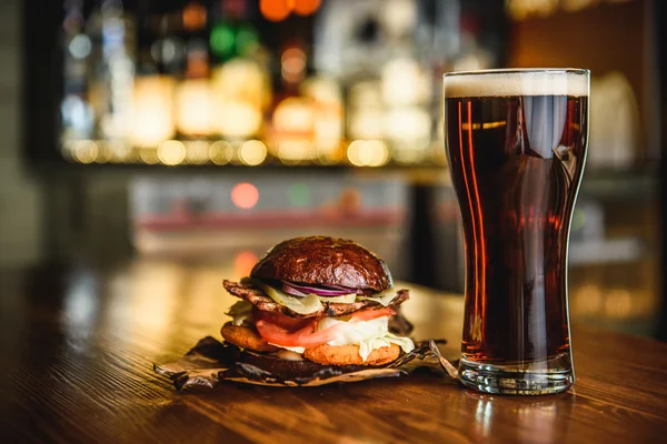 Hamburguesa y cerveza negra sobre fondo de pub . — Foto de Stock