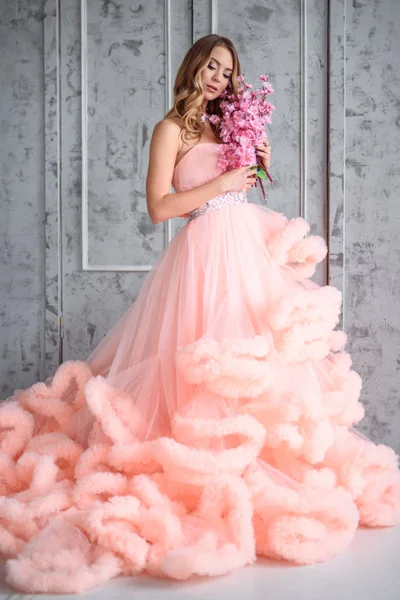 Bella ragazza con lunghi capelli ondulati in possesso di un mazzo di fiori in abito rosa la nuvola è al suo interno — Foto Stock